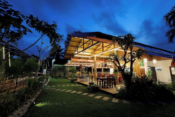 Un restaurante con patio al aire libre, terraza de madera y abundante vegetación.