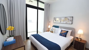 A hotel room with a bed, a nightstand, a desk, a lamp, a vase with flowers, and a window with curtains.