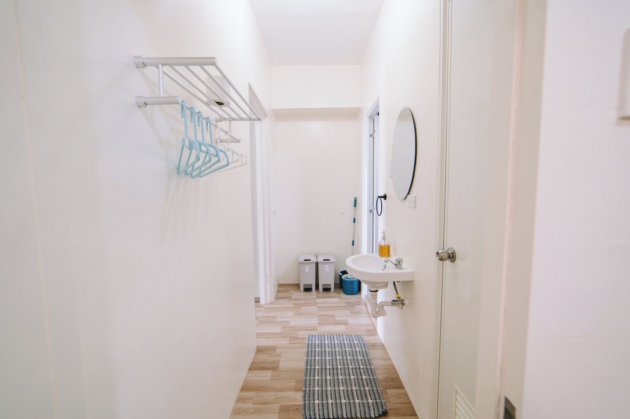 A narrow hallway with a white sink, mirror, and towel rack.