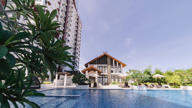 A modern hotel with a swimming pool, a well-maintained garden, and a tall building in the background. - APARTMENT IN LAPU-LAPU CITY RESORT TYPE-Near Mactan Airport 60 SQM.WITH 2BR (Lapu-Lapu)