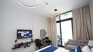 Ein modernes Hotelzimmer mit einem großen Bett, einem Schreibtisch mit Stuhl, einem an der Wand befestigten Fernseher und einem Balkon mit Vorhängen.