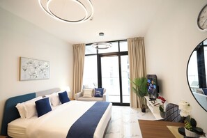Moderni hotellihuone, jossa on suuri sänky, työpöytä, jossa on televisio, tuoli ja suuri ikkuna.