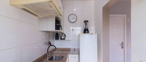 A compact kitchen with a gas stove, a sink, a blender, and a clock on the wall.