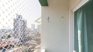 A balcony with a chain-link fence, a window with curtains, and a view of buildings in the background. - Apto 1 Quarto no centro em Itajaí CST0905 (Itajai)
