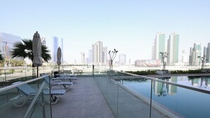 Ein Pool auf dem Dach mit Liegestühlen, einer Glasuferung und Blick auf die Stadtlandschaft.