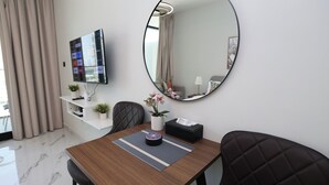 Ein modernes Hotelzimmer mit einem Holztisch, einem schwarzen Ledersessel, einem runden Spiegel, einem Flachbildfernseher und einer Topfpflanze.