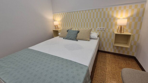 Ein Hotelzimmer mit einem Bett, zwei Nachttischen mit Lampen, einer karierten Wand und einem Teppichboden.