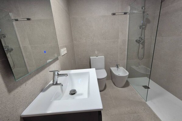 Un baño moderno con lavamanos blanco, inodoro, bidé y ducha con mampara de vidrio.