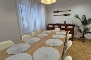 Un comedor con una mesa de madera larga, sillas blancas y posavasos redondos.