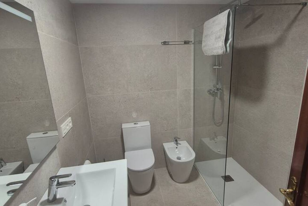 A bathroom with a toilet, bidet, sink, and glass shower enclosure.