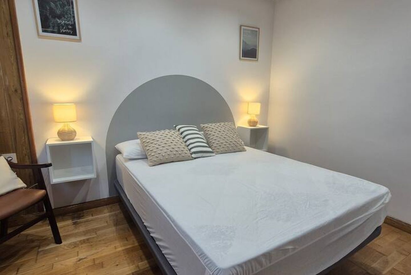 Ein Einzelbett mit geschwungener Kopfteile, zwei Nachttische mit Lampen, ein Holzstuhl und eine kleine Ablagefläche.