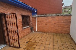 A courtyard with a tiled floor, a metal gate, a brick wall, and a blue roof.
