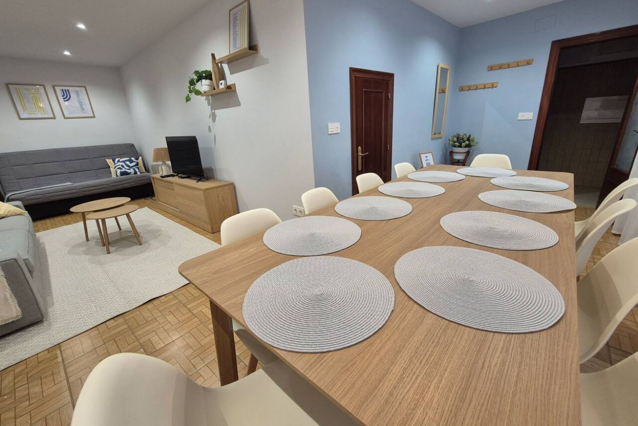 A modern dining area with a long wooden table, white chairs, and circular placemats.