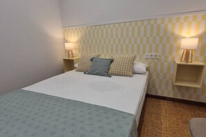 Una habitación de hotel con una cama, dos lámparas de noche, un papel tapiz a cuadros y suelo de madera.