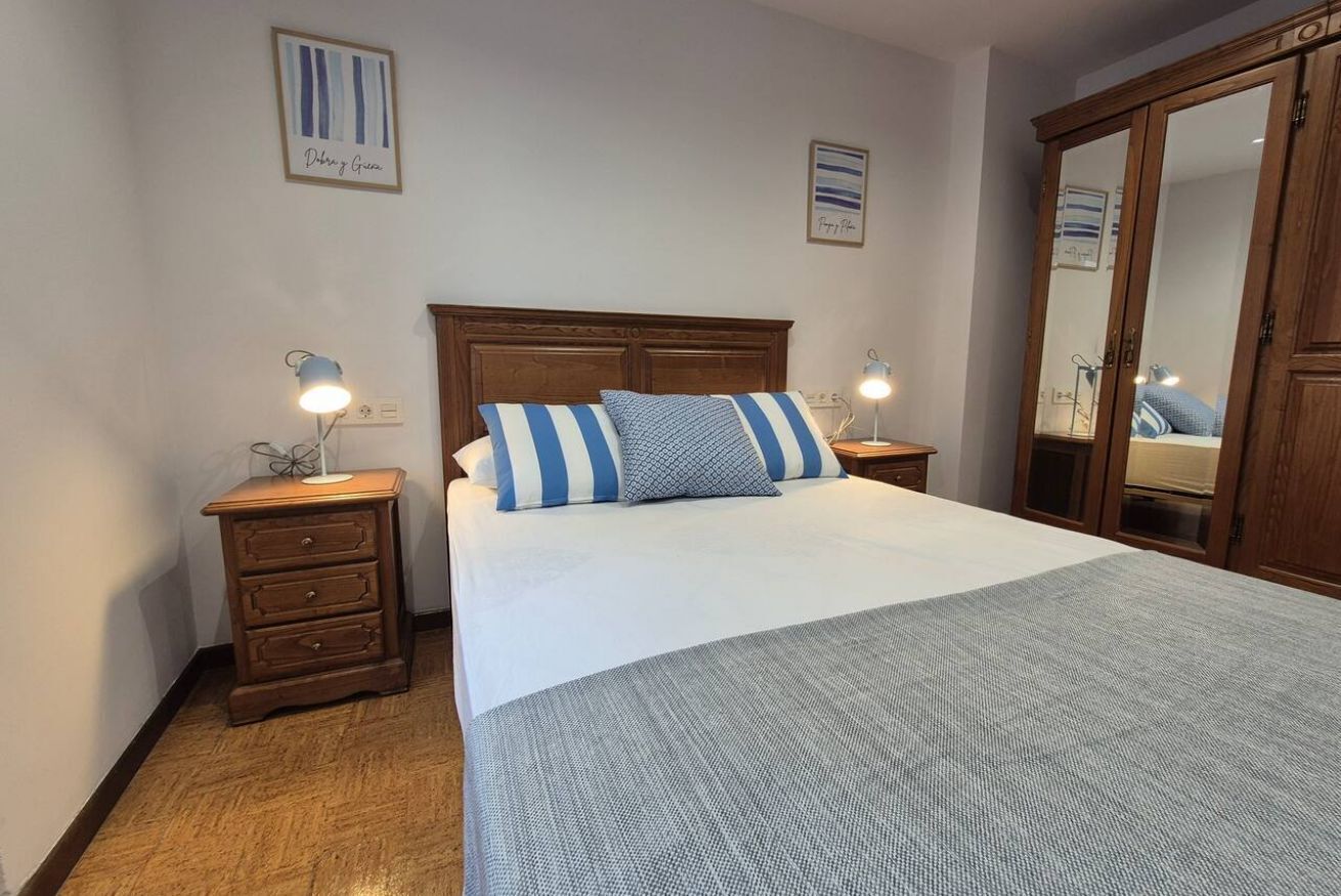 A bedroom with a wooden headboard, a bed with striped pillows, a bedside table with a lamp, a dresser, and a wardrobe.