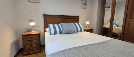 A bedroom with a wooden headboard, a bed with striped pillows, a bedside table with a lamp, a dresser, and a wardrobe.