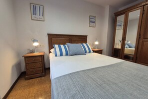 Un dormitorio con cabecera de madera, cama con almohadas a rayas, mesita de noche con lámpara, cómoda y armario.