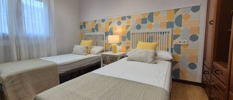 A hotel room with two single beds, a bedside table with a lamp, a radiator, and a wardrobe.