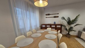 Ein Esszimmer mit Holztisch, weißen Stühlen, einer Pendelleuchte, einem Blumentopf und einem Wanddekor.