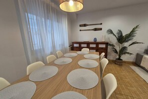 Comedor con mesa de madera, sillas blancas, lámpara colgante, planta en maceta y un adorno en la pared.