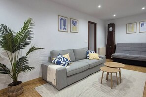 Una sala de estar con un sofá gris, una mesa de centro, una planta en maceta y un reloj en la pared.