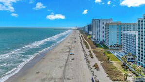 A coastal hotel with a beach view, multiple floors, and a long promenade along the shore.
