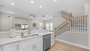 A modern kitchen with white cabinetry, a dishwasher, and a wooden staircase.