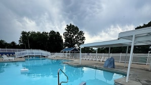 A swimming pool with a white fence, lounge chairs, and a covered area.