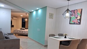 Un salon moderne avec un canapé gris, un coin repas avec une table et des chaises, et une cuisine en arrière-plan.