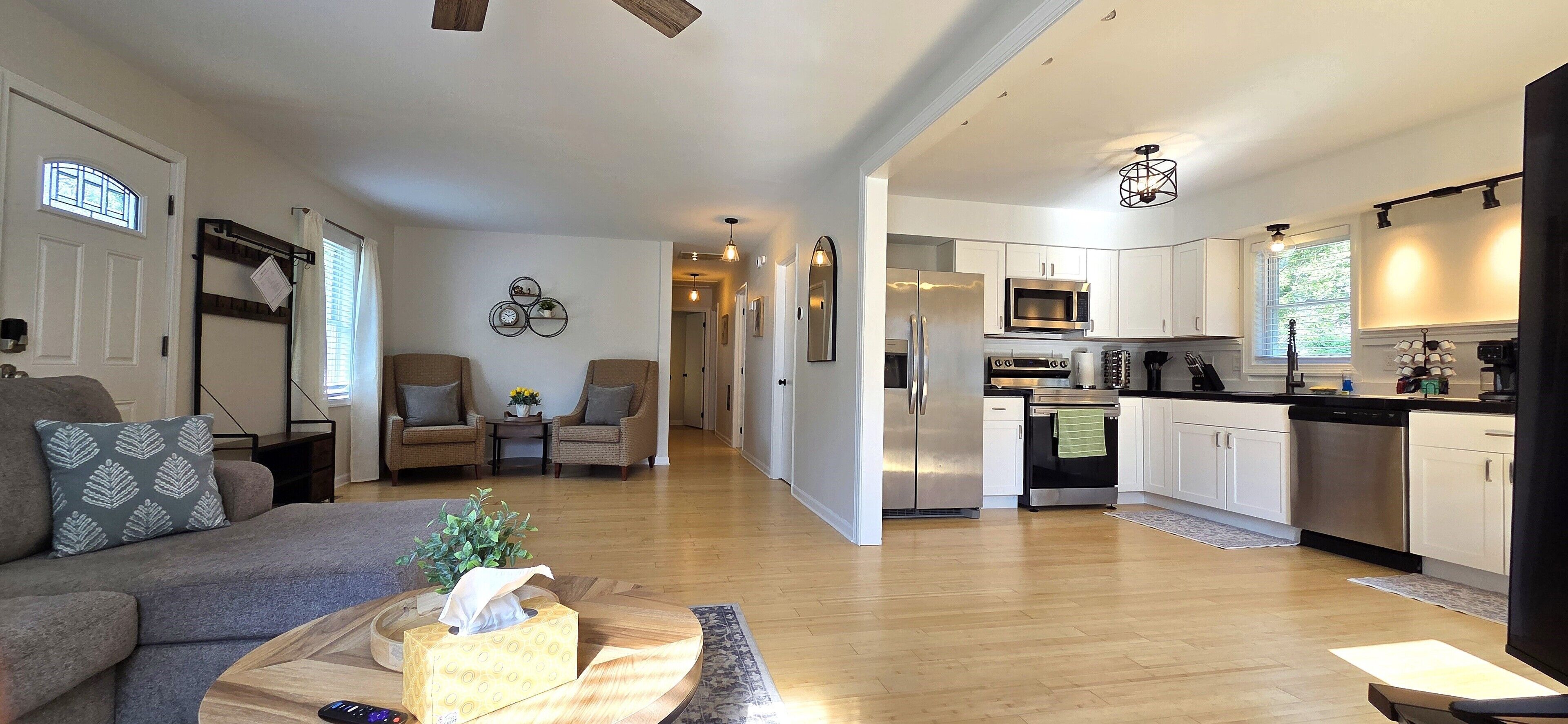 A modern kitchen with stainless steel appliances, a dining area with a sofa and chairs, and a hallway leading to another room.