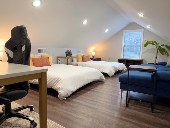 A modern, well-lit room with two beds, a desk, a chair, and a blue sofa.
