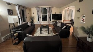Ett vardagsrum med två soffor, ett soffbord och en tv. En matplats med ett bord och stolar syns genom en öppning i väggen.