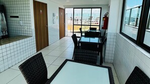 A dining area with a table and chairs, a kitchen area with a refrigerator, and a view of the city through large windows. - Apartment 350 meters from the shopping mall (Boa Viagem Recife)