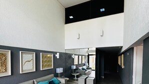 A spacious living area with a grey sofa, a coffee table, and a TV. There are framed artworks on the wall and a staircase leading to an upper level. - Apartment 350 meters from the shopping mall (Boa Viagem Recife)