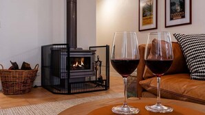 Un accogliente soggiorno con camino, due bicchieri di vino rosso, un cesto di vimini e un cuscino decorato su un divano in pelle.