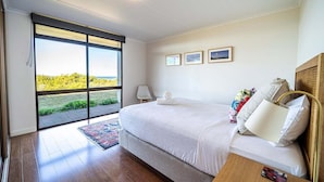 Una camera da letto con un grande letto, vista attraverso una porta scorrevole in vetro e un piccolo comodino.