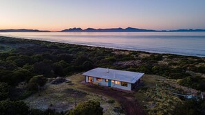 Una casa moderna con tetto piatto, immersa nella macchia mediterranea e con una distesa d'acqua sullo sfondo.