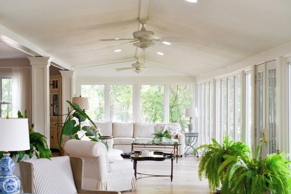 Una habitación amplia con ventilador de techo, un sofá, una mesita de centro y ventanas grandes.