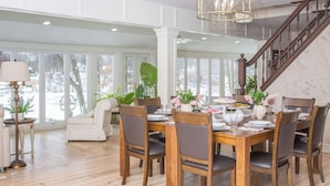 A dining area with a wooden table set for six, surrounded by chairs, with a staircase in the background. - Lakefront Estate w/ Beach & Boat • Sleeps 30 • Near IN Dunes National Park (Valparaiso)