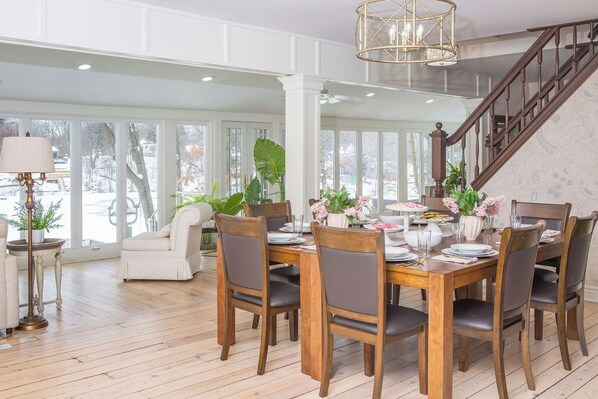 A dining area with a wooden table set for six, surrounded by chairs, with a staircase in the background.