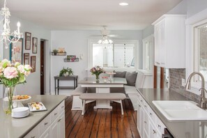 Una cocina moderna con una isla central, muebles blancos y una zona de comedor con banco.