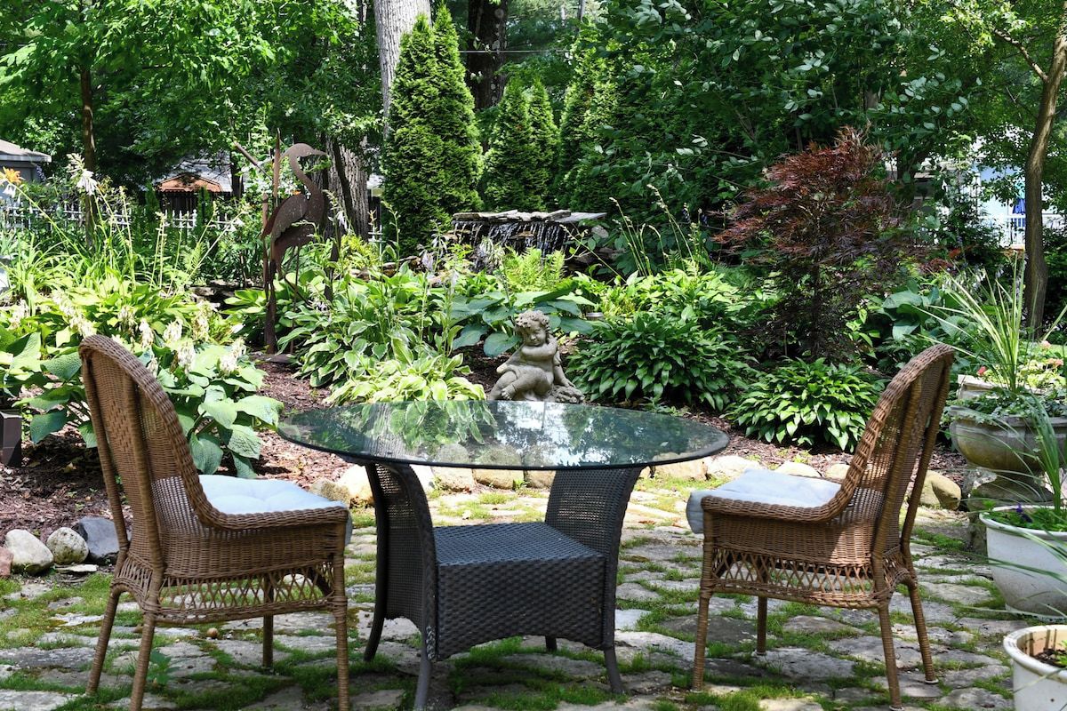 Een tafel met glazen blad en twee rieten stoelen in een tuin.