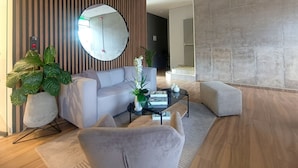 Una sala de estar moderna con un sofá blanco, un espejo redondo, una mesa de centro de vidrio y una planta grande en maceta.