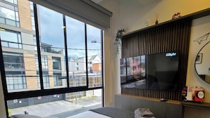 Una habitación de hotel moderna con una cama grande, una televisión y vistas de la ciudad a través de amplios ventanales.
