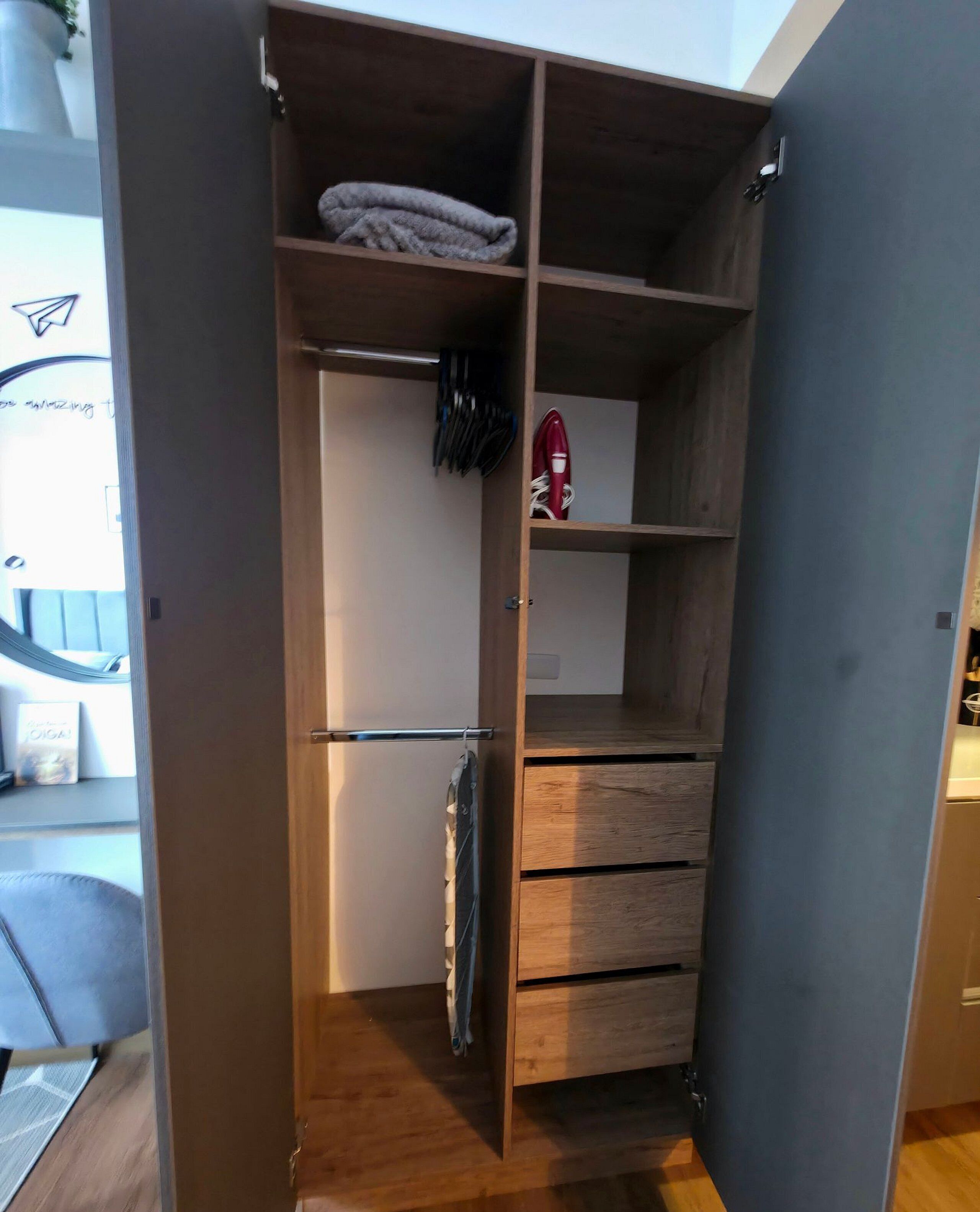 Un armario de madera con varios compartimentos, una barra para colgar y un electrodoméstico rojo.