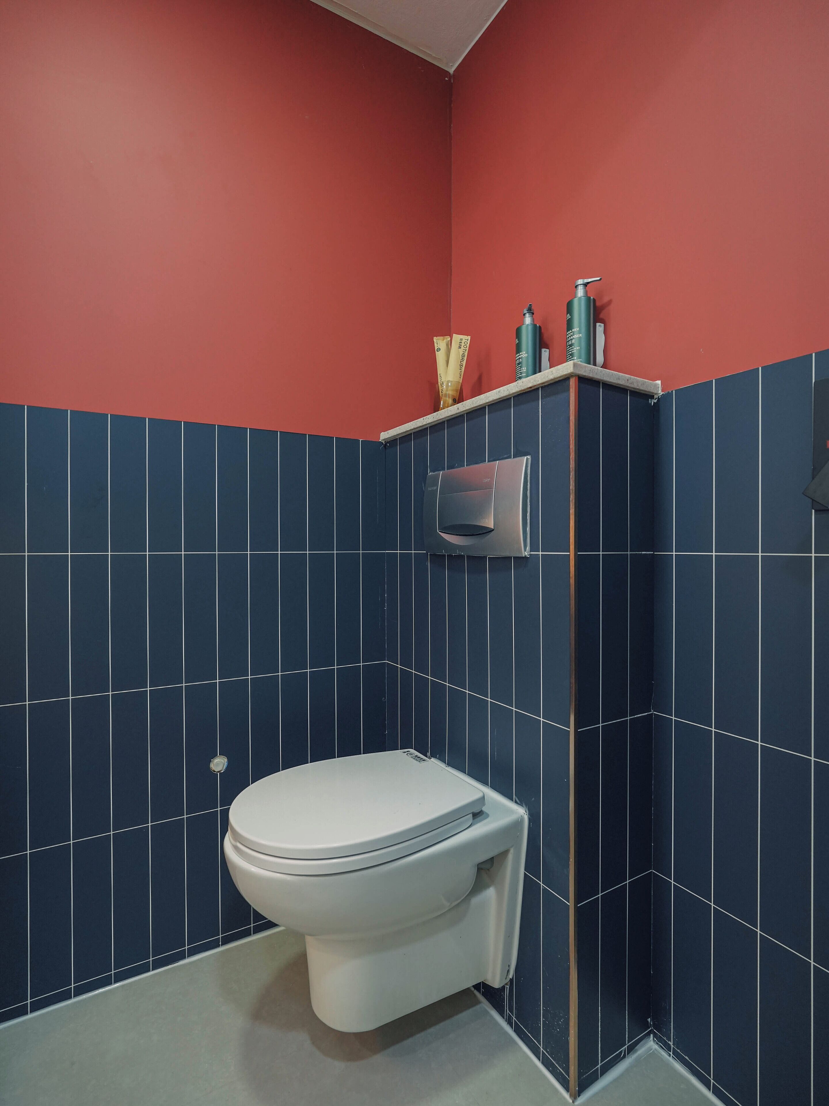 Un baño con inodoro blanco, paredes con azulejos azules y una pared de acento roja.