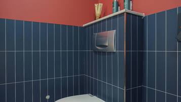 Un baño con inodoro blanco, paredes con azulejos azules y una pared de acento roja.