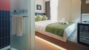 Hotelkamer met een bed, een groene plaid, een handdoek op het bed, een nachtkastje met een telefoon, en een raam met gordijnen.