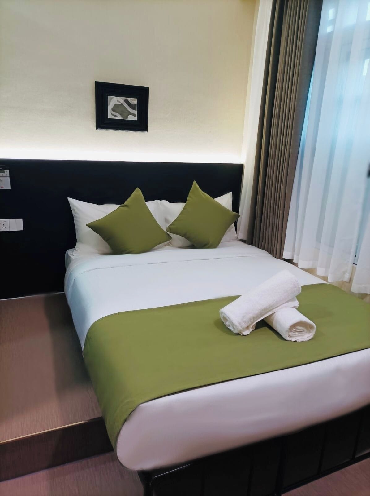 Una cama bien hecha con ropa de cama blanca y verde, dos almohadas y una toalla blanca enrollada.