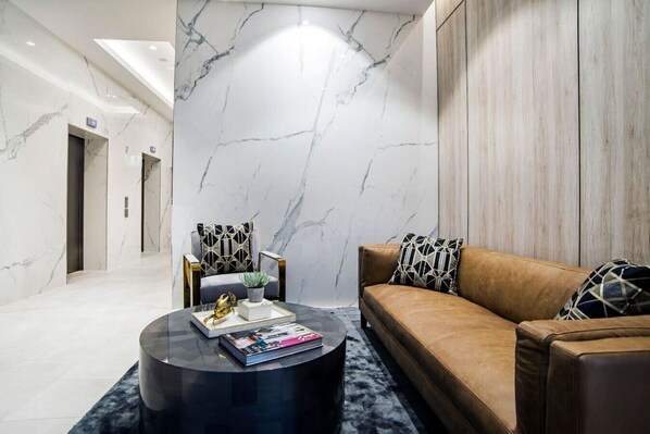 A modern lobby with a marble wall, a leather sofa, and a round coffee table with magazines.